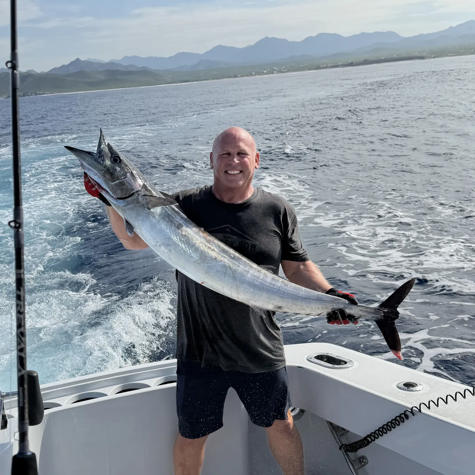 Guest holding a wahoo on the stern with the coastline astern