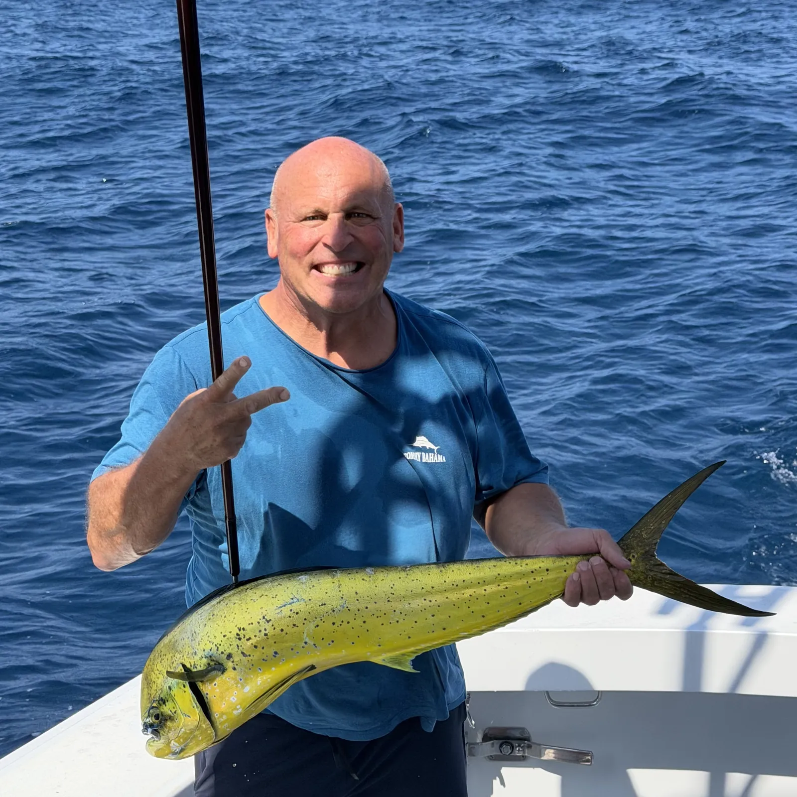 Two guests showing off a dorado on the stern with the Baja coastline behind