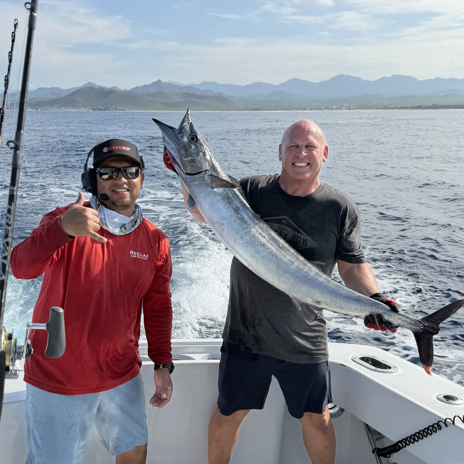 Two guests holding a wahoo with the Baja mountains behind