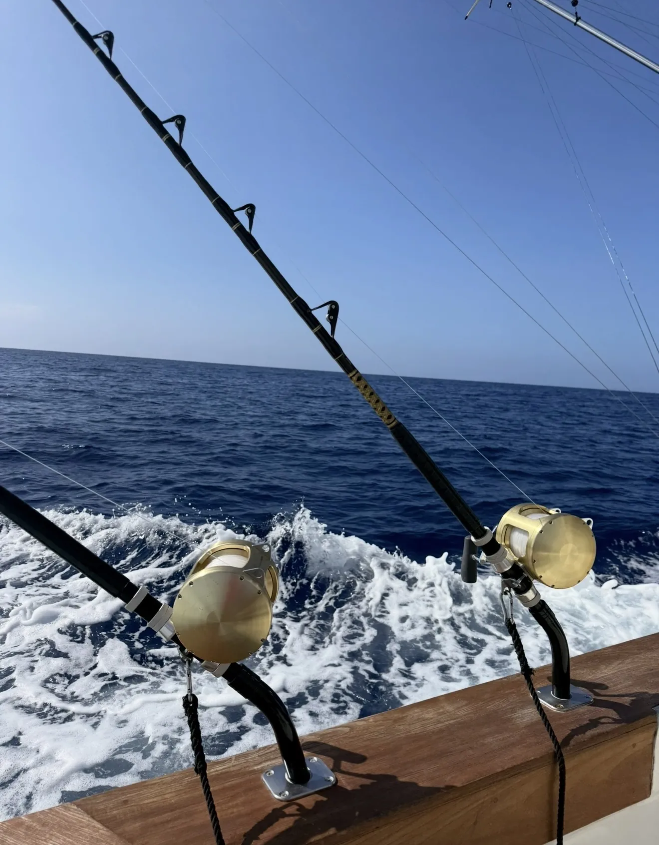 Tournament-grade trolling rods and gold reels set in the teak rail